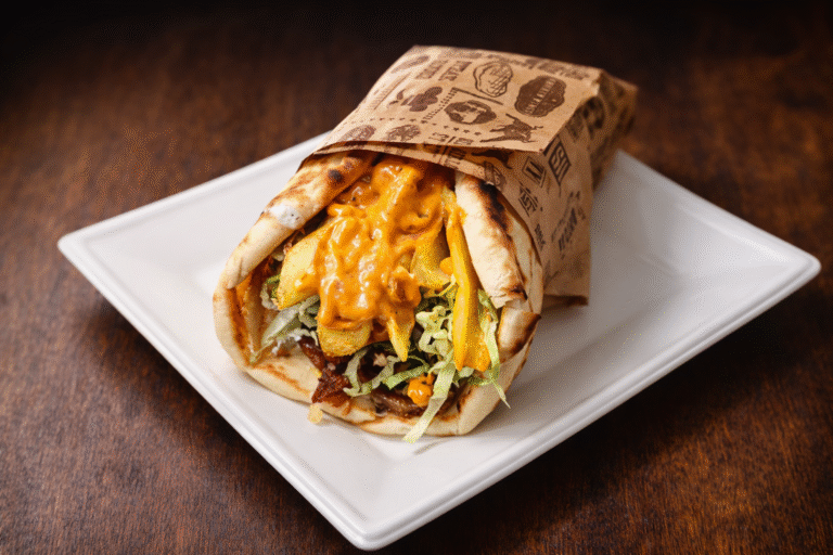 A Mondo Trio gyros pitája fehér tányéron, fa háttér előtt – AI segítségével átdolgozott étlapkép.