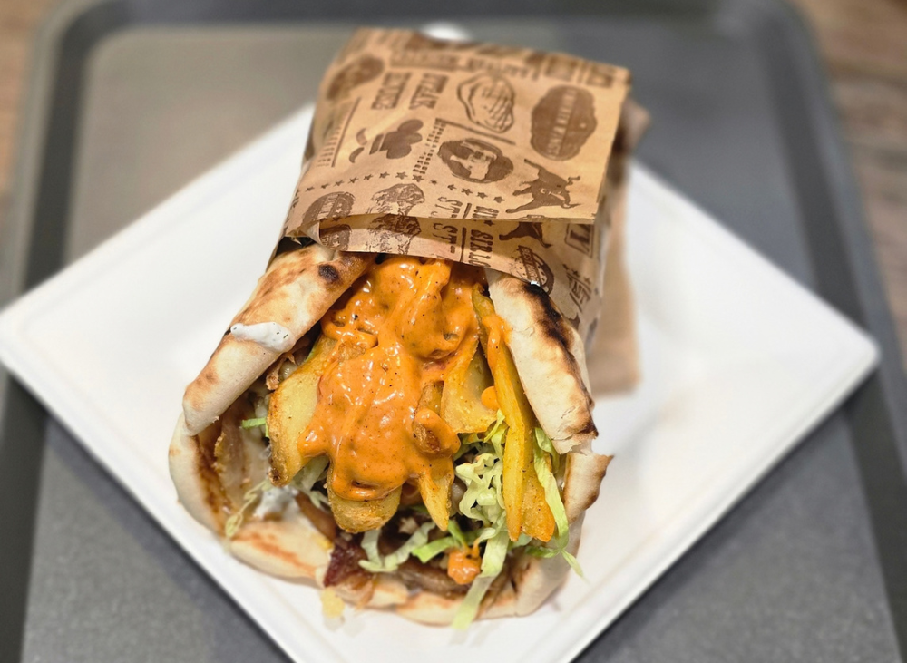 Mondo Trio gyros pita papírcsomagolásban, fehér tányéron – eredeti ételfotó.